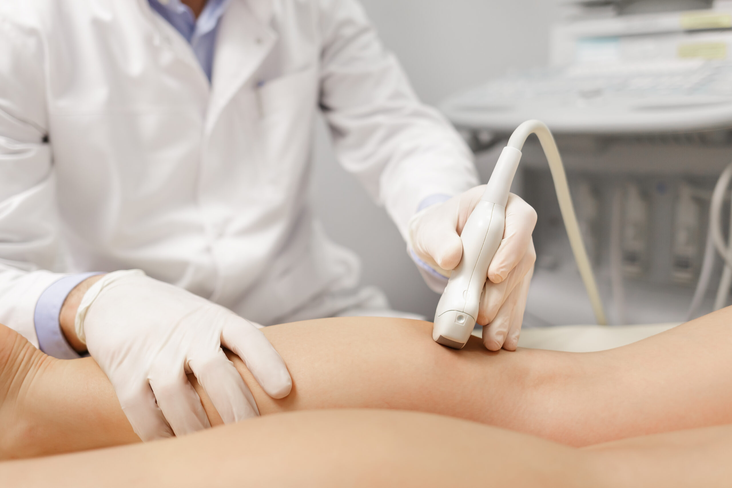 Orthopedist doctor doing ultrasound examination of patient's leg veins in his office. Young woman passing ultrasound scan in clinic. Doctor work. Medical research.